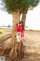 A woman leaning against a tree on the beach.