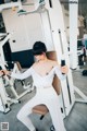 A woman in a white top and white pants working out in a gym.