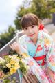 A woman in a kimono sitting on a bench with flowers.