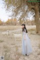 A woman in a blue dress standing in front of a herd of goats.