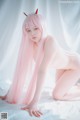 A woman with long pink hair is posing naked on a bed.