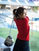 A woman in a red sweater and plaid skirt holding a golf club.