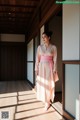 A woman in a pink kimono standing in a room.