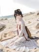 A woman in a white dress sitting on a sandy beach.