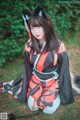 A woman in a black and red kimono sitting in the grass.