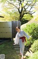 A woman in a blue and white kimono standing in a garden.